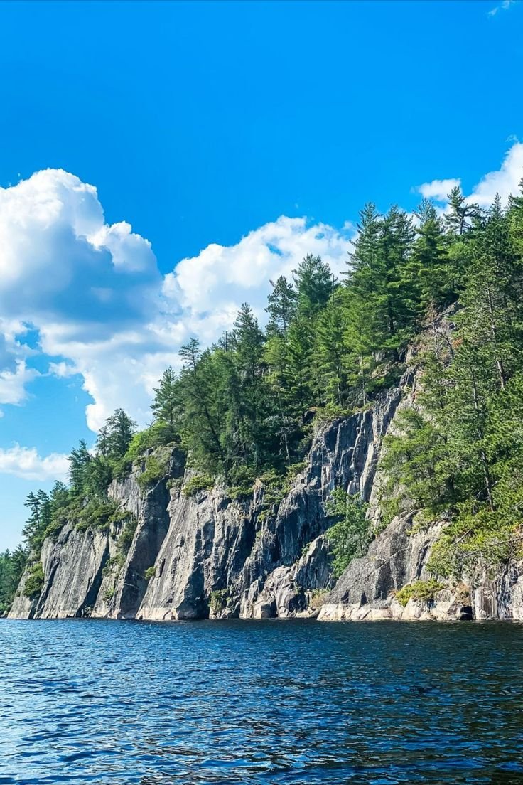 This may contain: a boat is on the water near some cliffs and trees in the distance with blue skies above