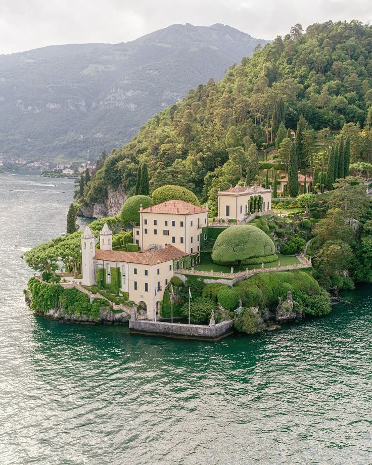 This may contain: an island in the middle of water surrounded by trees and bushes with buildings on it