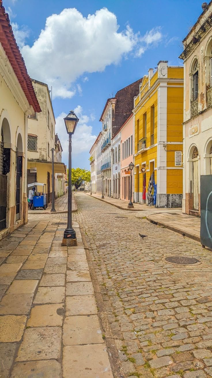 This may contain: an empty street lined with colorful buildings under a blue sky