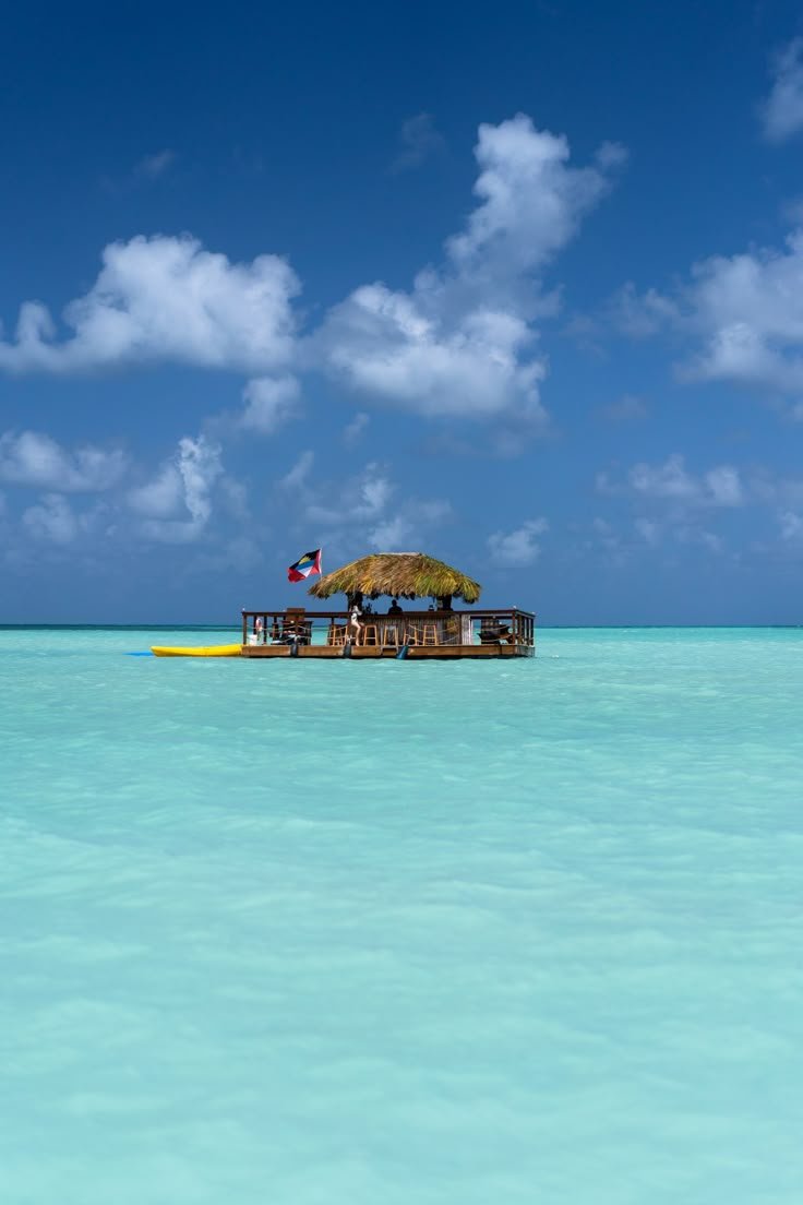 This may contain: a house on stilts in the middle of clear blue water with clouds above it