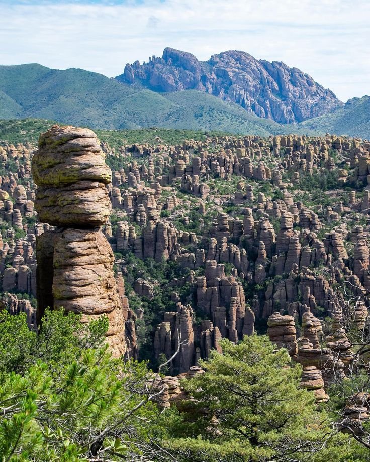 This may contain: the rocks are stacked high up in the trees and mountains behind them, as if they were rock formations