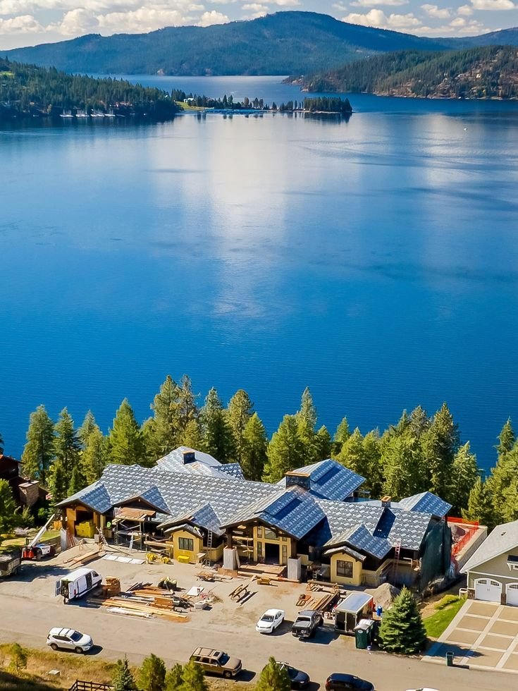 This may contain: an aerial view of a large lake surrounded by trees and buildings with mountains in the background