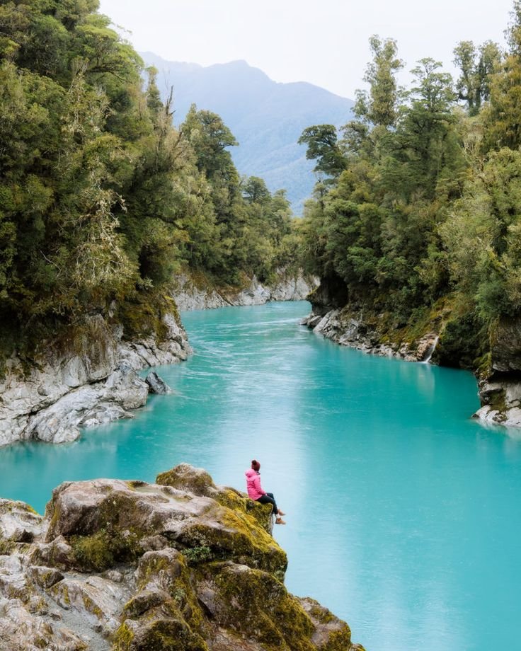This may contain: a person sitting on top of a rock next to a river