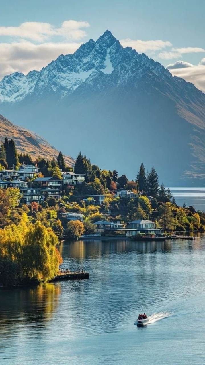 This may contain: a small boat is on the water in front of some mountains and houses with snow capped peaks