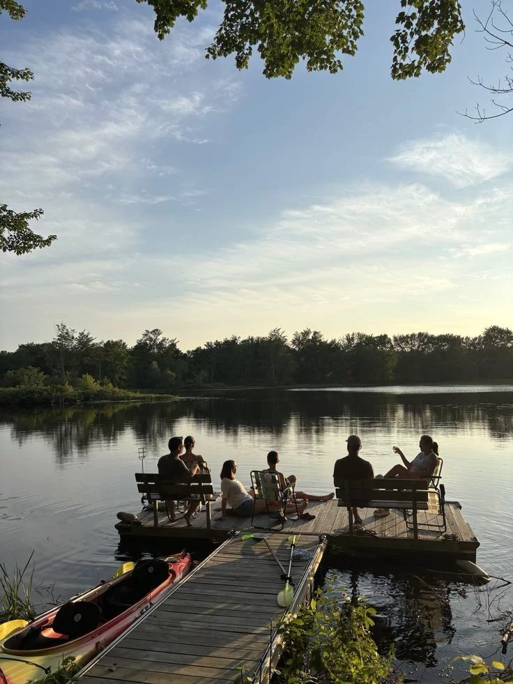 This may contain: several people sitting on benches at the end of a dock near a body of water