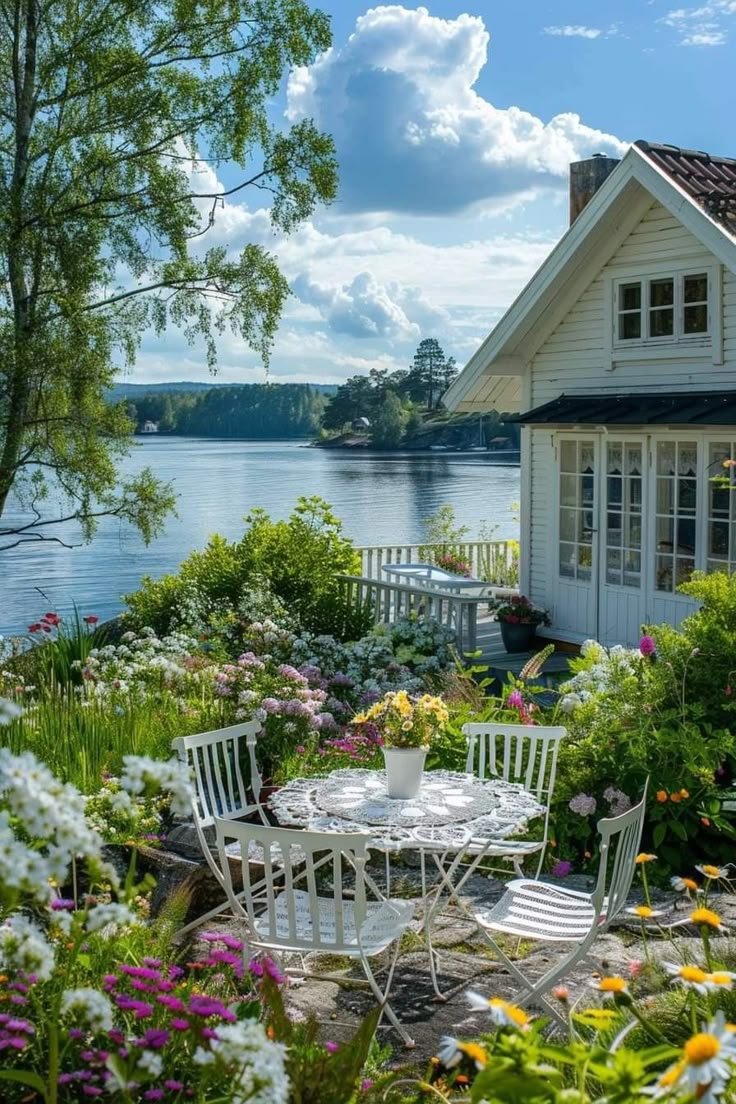 This may contain: a white table and chairs sitting in front of a house next to the water on a sunny day