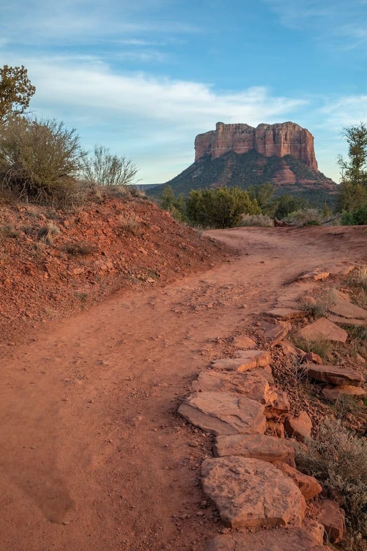 This may contain: a dirt road with rocks on both sides and a mountain in the distance behind it