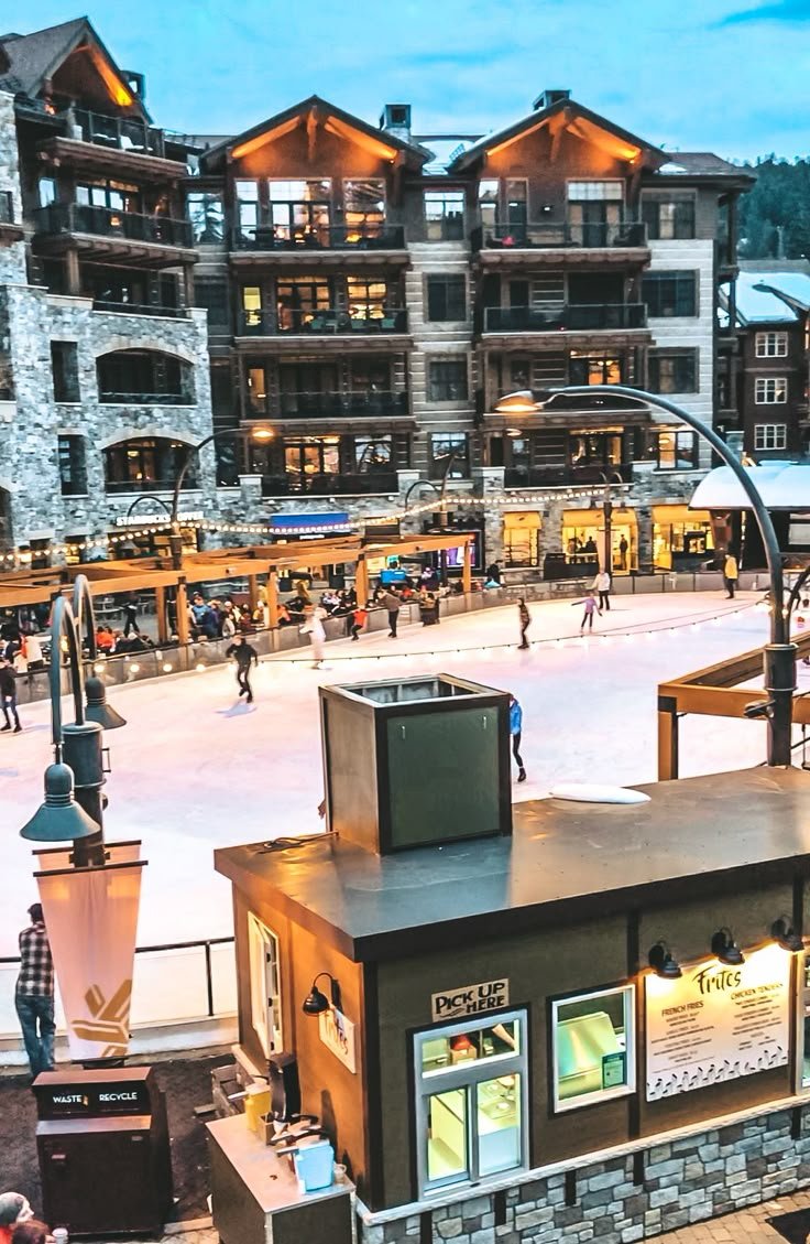 This may contain: an outdoor ice rink with people skating on it and buildings in the background at dusk