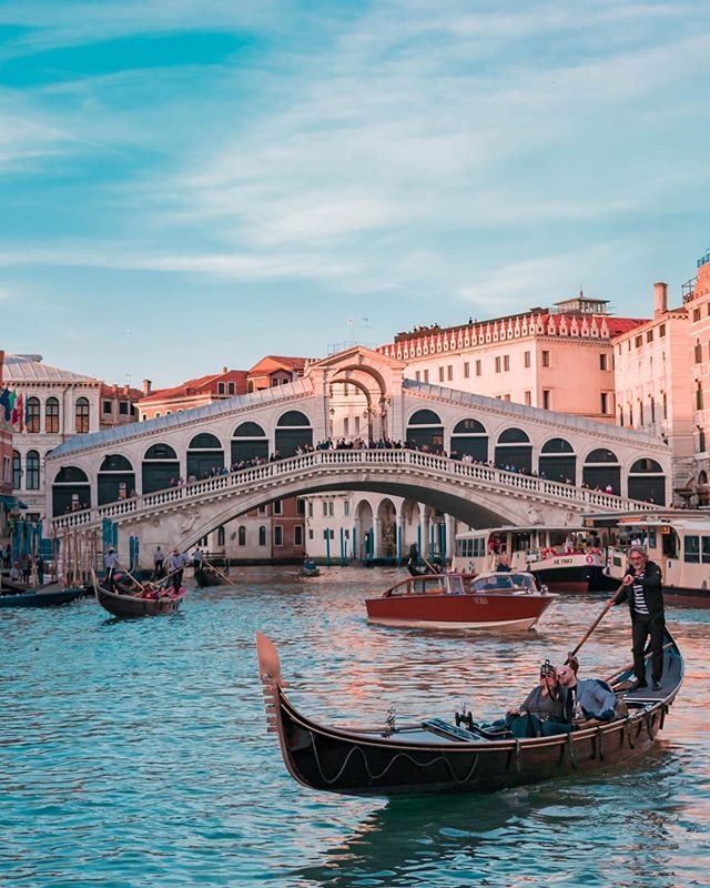 This may contain: two gondolas in front of a bridge with people riding on one and another boat