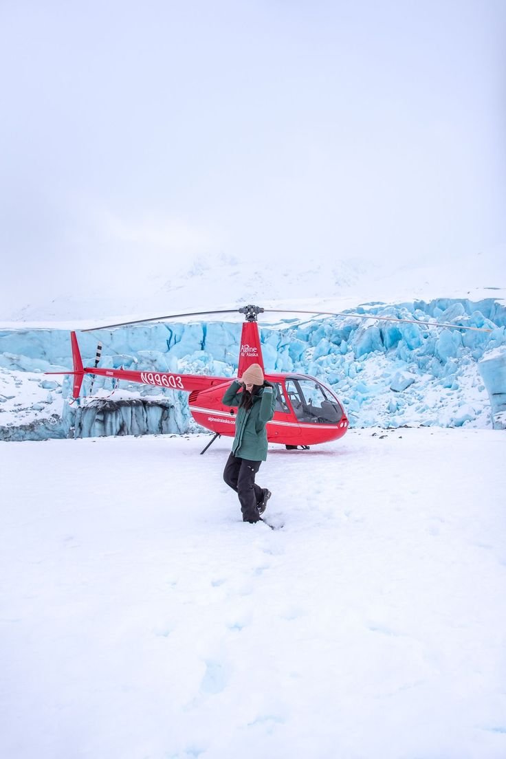 This may contain: a man standing in the snow next to a helicopter