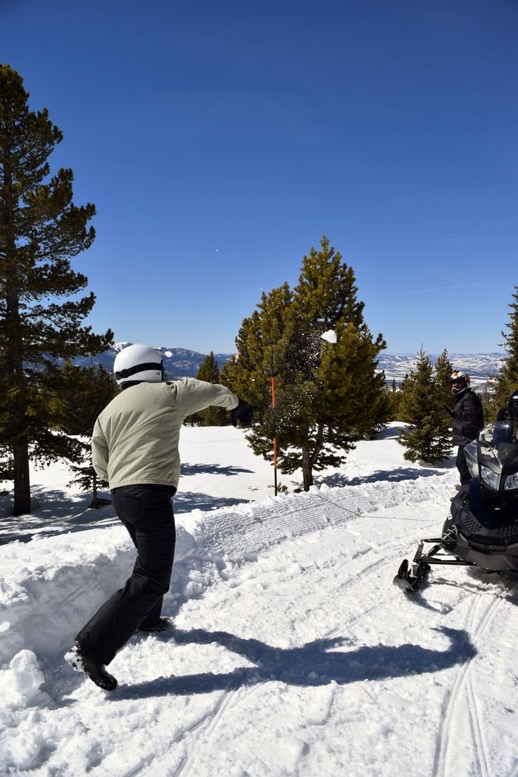 This may contain: a man riding a snowmobile down a snow covered slope next to a person on a sled