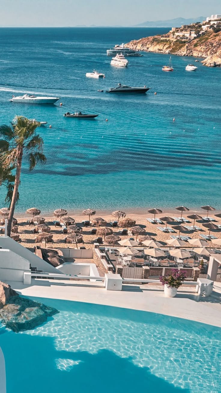 This may contain: an outdoor swimming pool next to the beach with boats in the water and palm trees