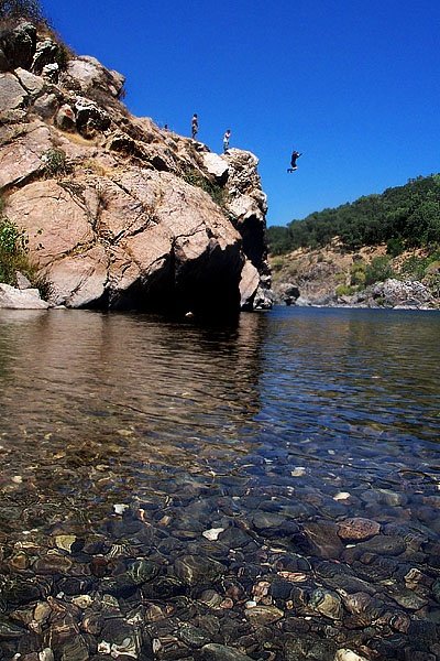 This may contain: some people are standing on rocks in the middle of a body of water with clear blue skies above