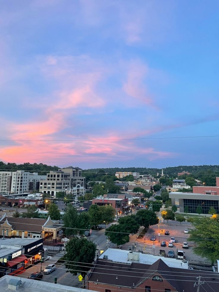 This may contain: the sky is pink and blue as the sun goes down in this cityscape