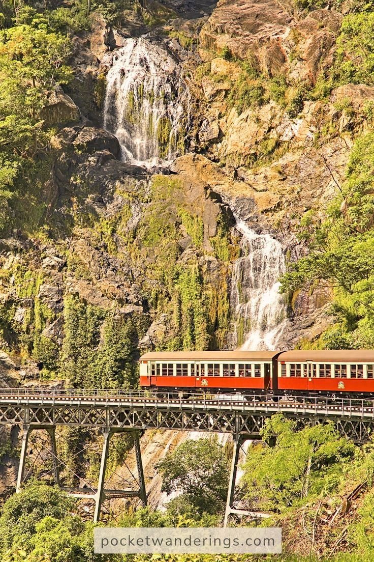 This contains: A vintage red train crosses a scenic bridge with a cascading waterfall in the background, showcasing one of the most beautiful train journeys in the world.