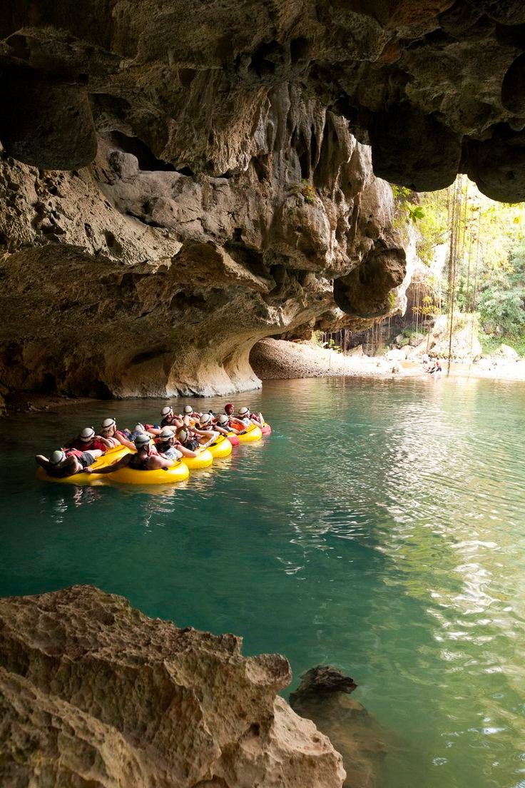 This may contain: a group of people riding on top of yellow rafts down a river under a cave