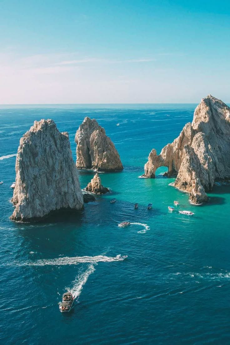 This may contain: several boats are in the water near large rocks