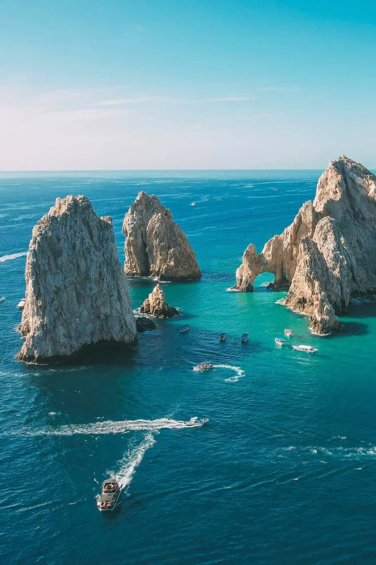 This may contain: several boats are in the water near large rocks