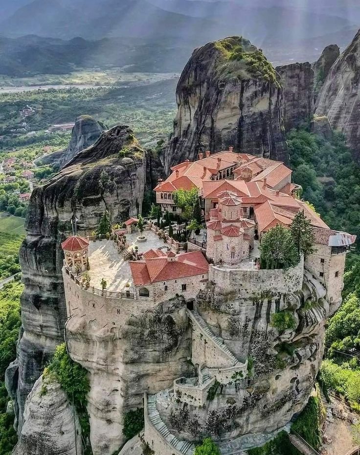 This may contain: an aerial view of a castle on top of a mountain with trees and mountains in the background