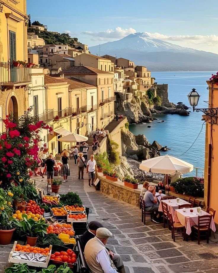 This may contain: people are sitting at tables on the side of a street with flowers and fruit in front of them