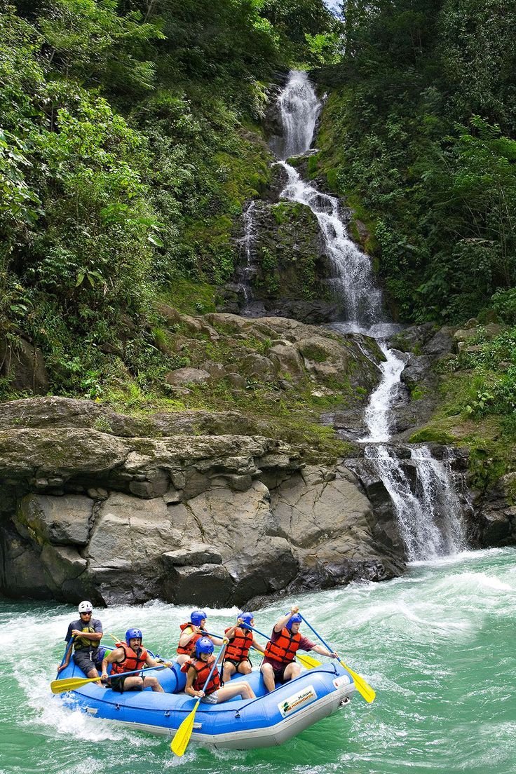 This contains: A group in an inflatable boat white water rafting on the Pacuare River in Costa Rica with a small waterfall in the background