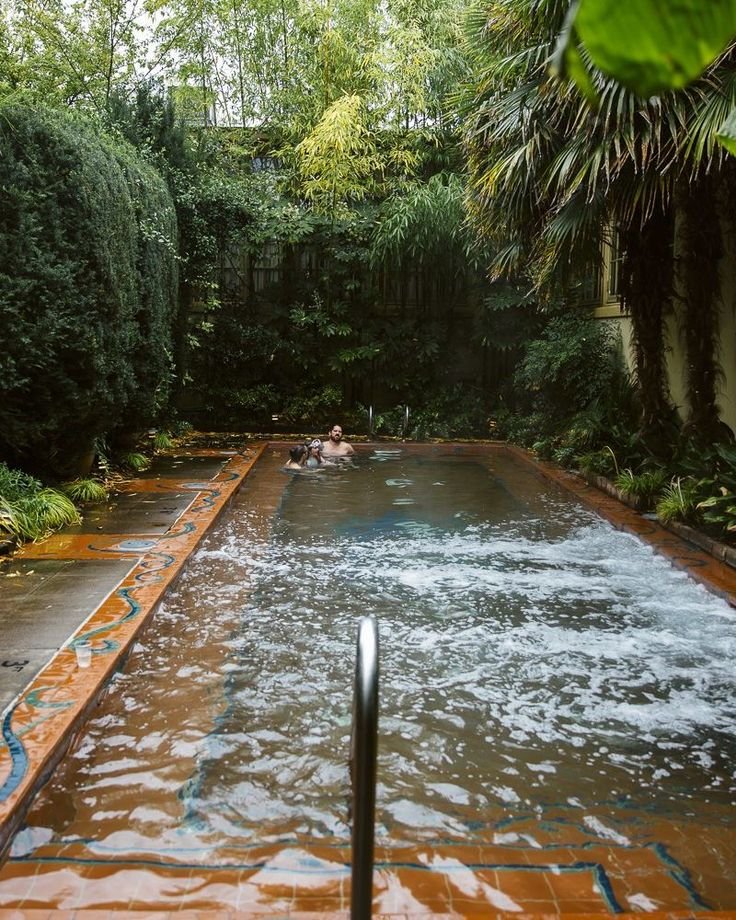 This may contain: an outdoor hot tub surrounded by trees and plants