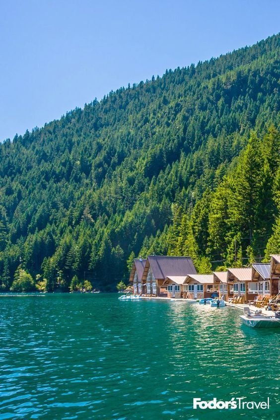 This may contain: boats are parked on the water in front of some houses and mountains with trees around them