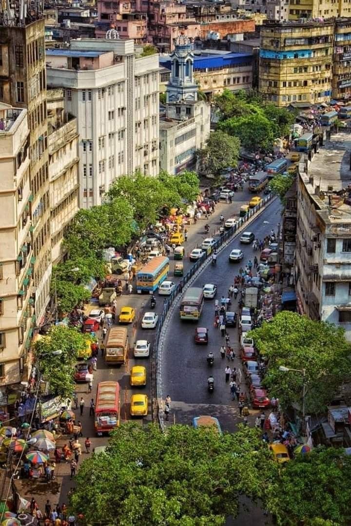This may contain: a city street filled with lots of traffic next to tall buildings and green leafy trees