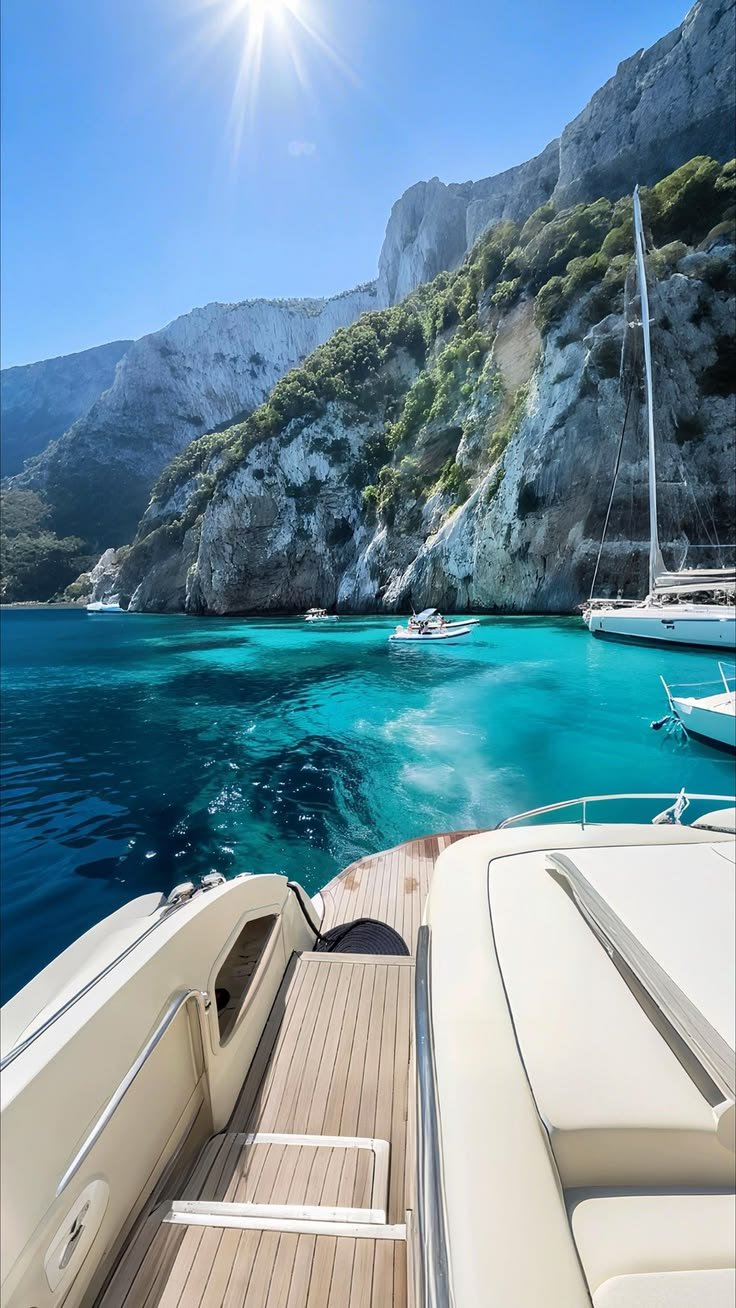 This may contain: the sun shines brightly over blue water and boats docked in front of some cliffs