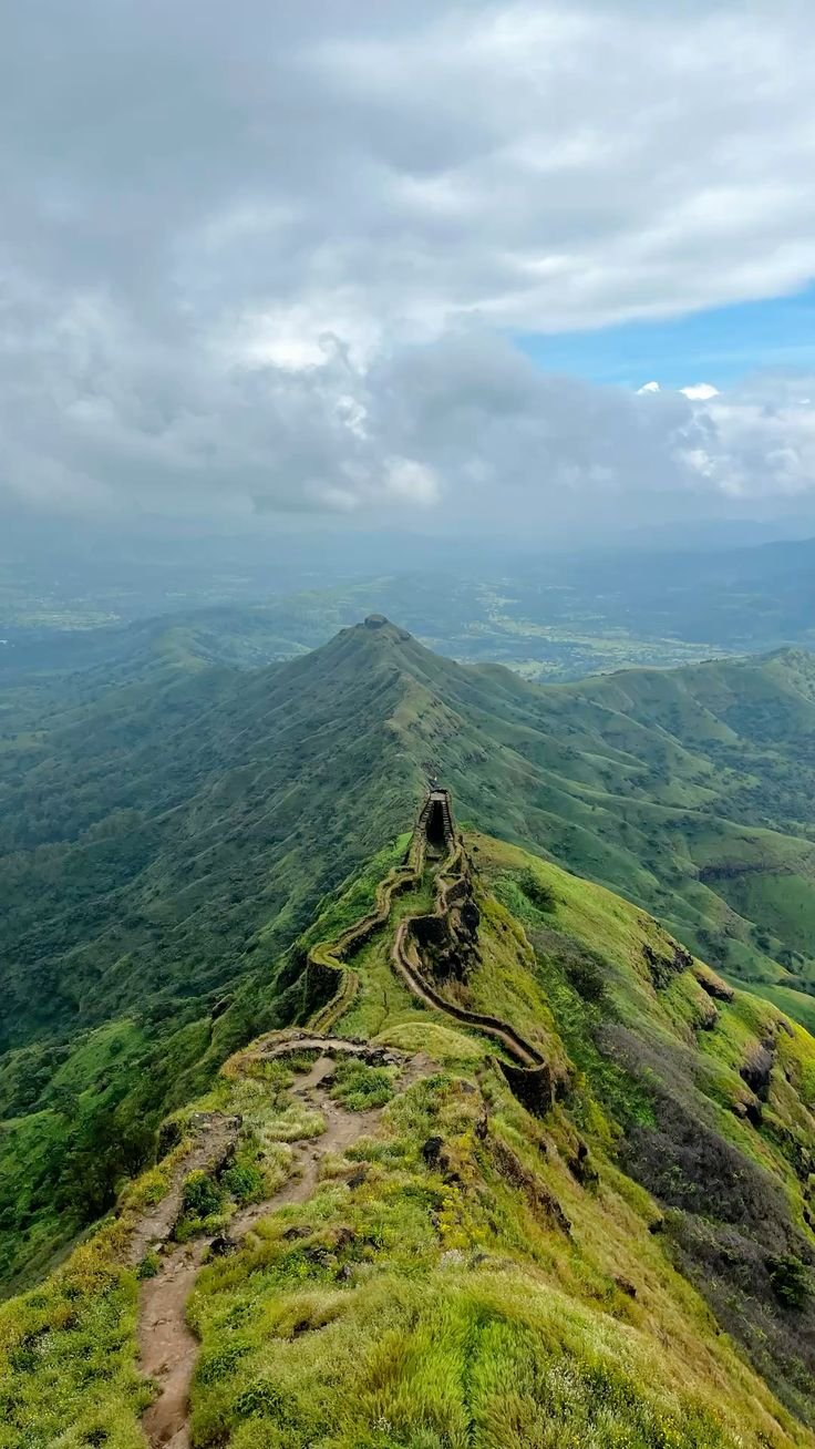 This may contain: a view from the top of a mountain with green grass and mountains in the background