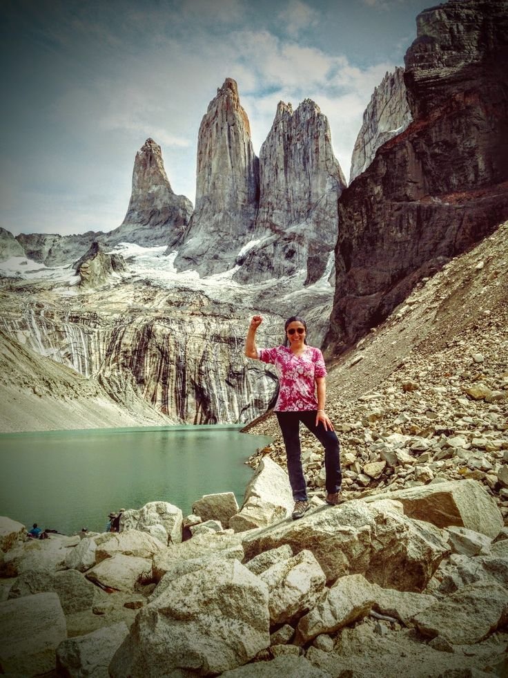 This may contain: a woman standing on top of a rocky mountain next to a lake