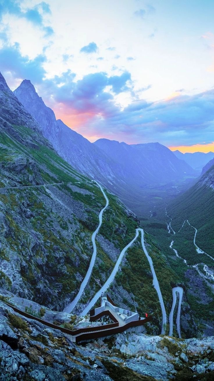 This may contain: an aerial view of a winding road in the mountains at sunset, with cars driving on it