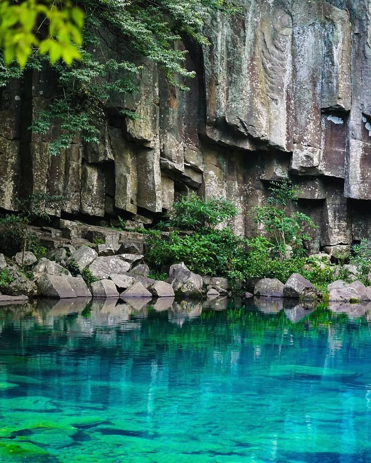 This may contain: the water is crystal blue and green in this cave like area with rock formations on either side