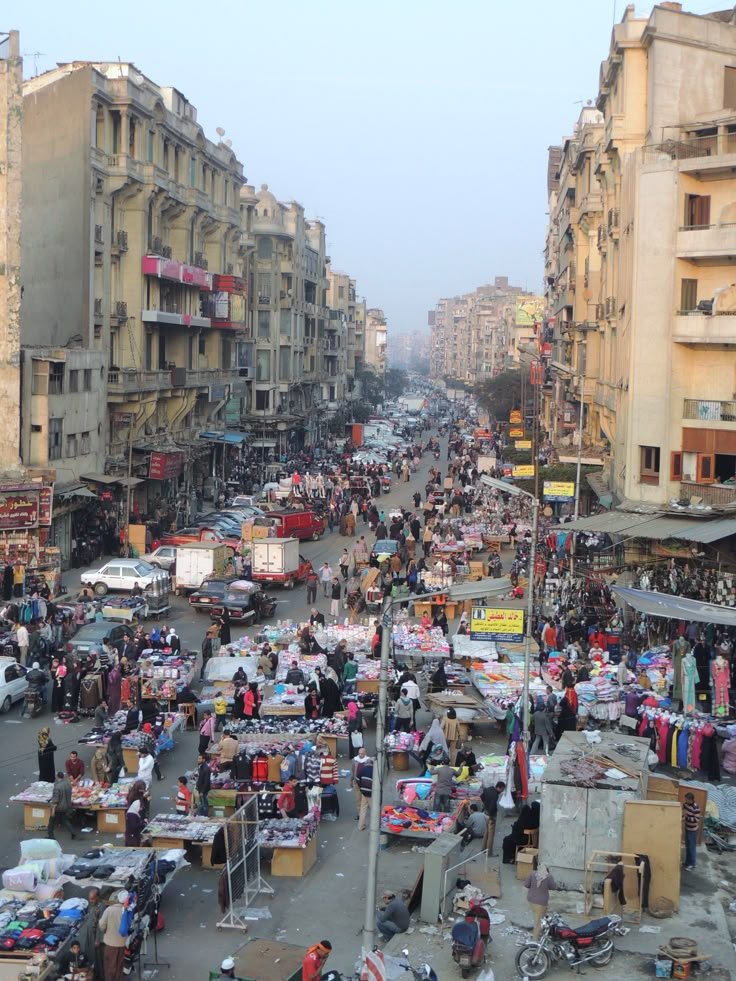 This may contain: a busy street with lots of people walking around and cars parked on the side of it