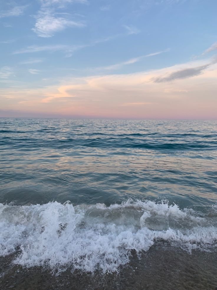 This may contain: the ocean waves are coming in to shore as the sun is setting on the horizon