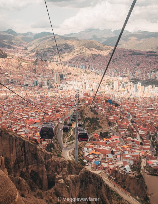 This may contain: a cable car going over a large city with mountains in the backgrouds