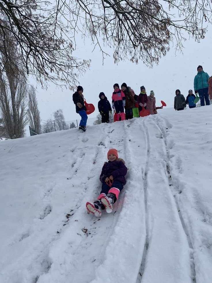 This may contain: a small child is sledding down a hill with people watching from the side