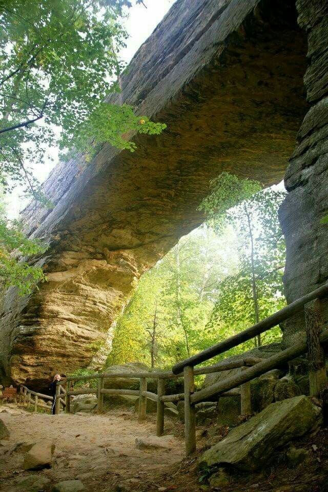 This may contain: a person standing under an overhang in the woods near a rock formation and stairs