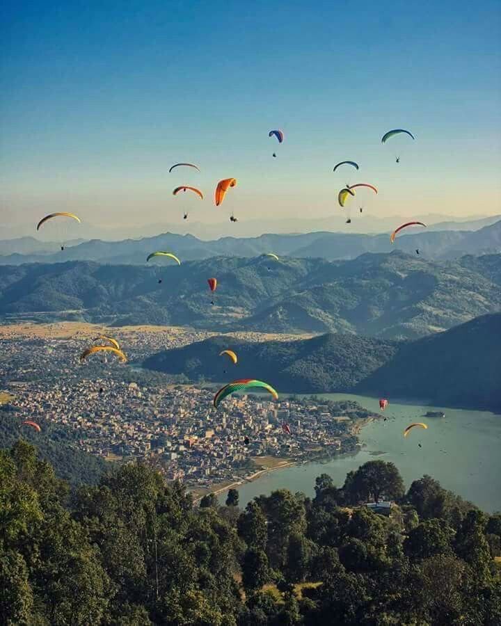 This may contain: many colorful kites are flying in the sky over a city and lake with mountains in the background