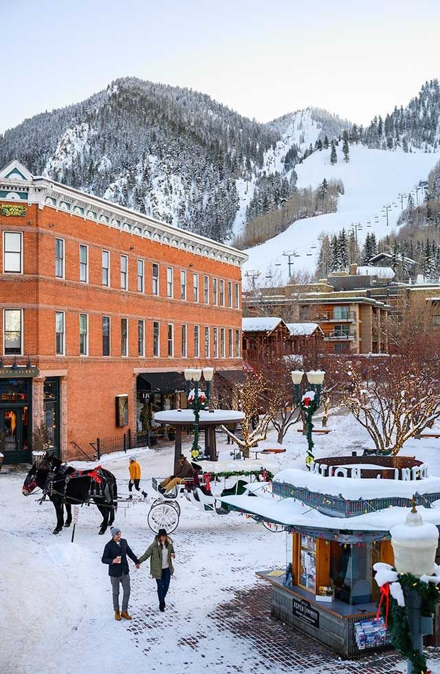 This may contain: people are walking through the snow in front of a building with mountains in the background