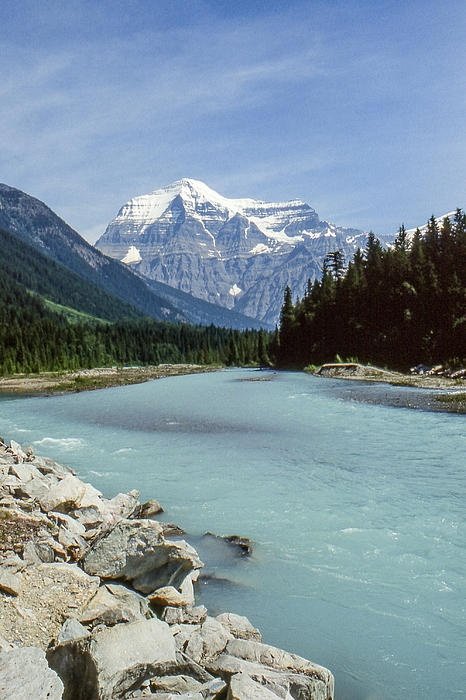 This may contain: there is a mountain range in the background with blue water and rocks on the shore