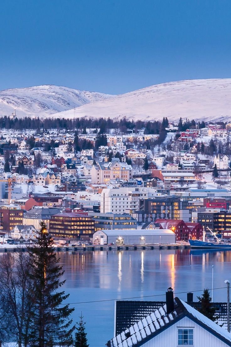 This may contain: the city is surrounded by snow covered mountains and water, with houses on either side