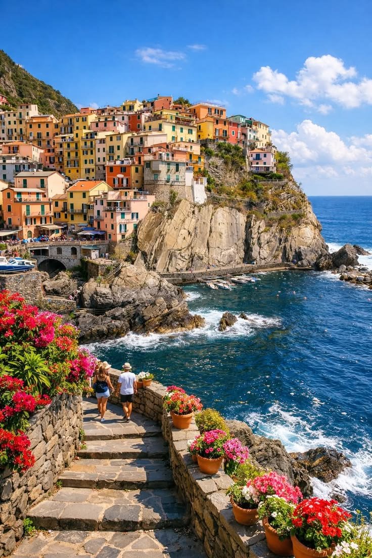This may contain: some people are walking up the steps to an ocean side town with colorful flowers on it
