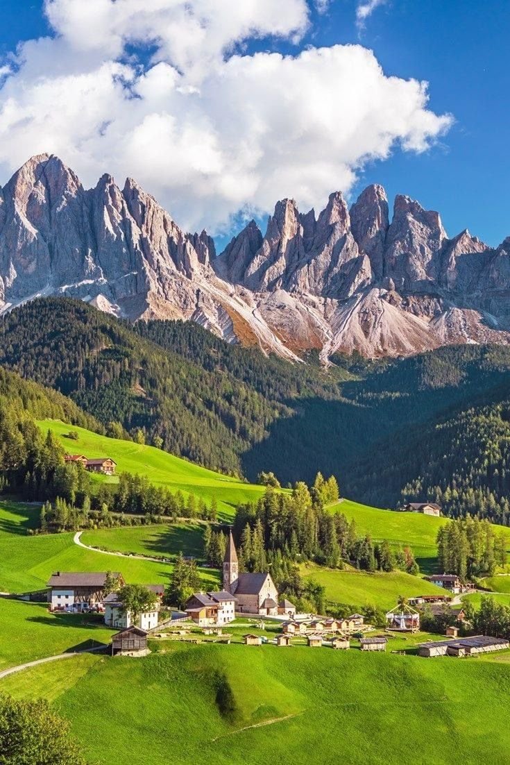 This may contain: the mountains are covered with green grass and houses in the foreground, surrounded by lush greenery