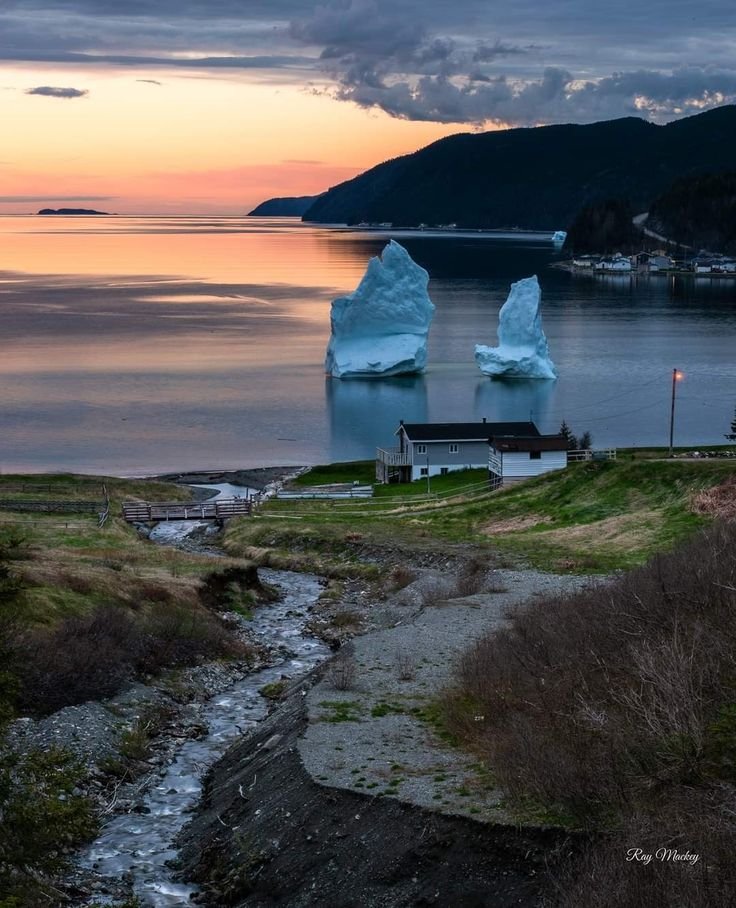 This may contain: two icebergs are in the water at sunset near a small house and some hills