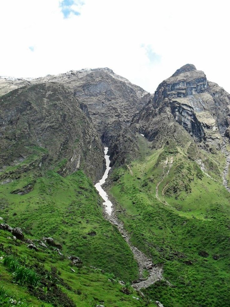 This may contain: the mountains are covered with green grass and water flowing from them to the river below
