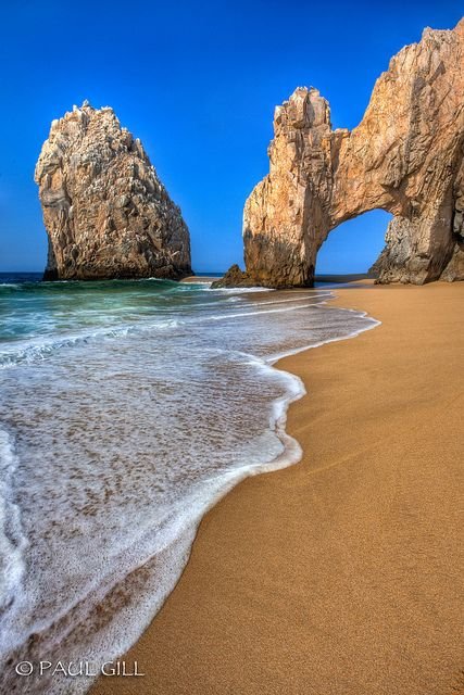 This may contain: two large rocks sticking out of the ocean next to a sandy beach with waves coming in