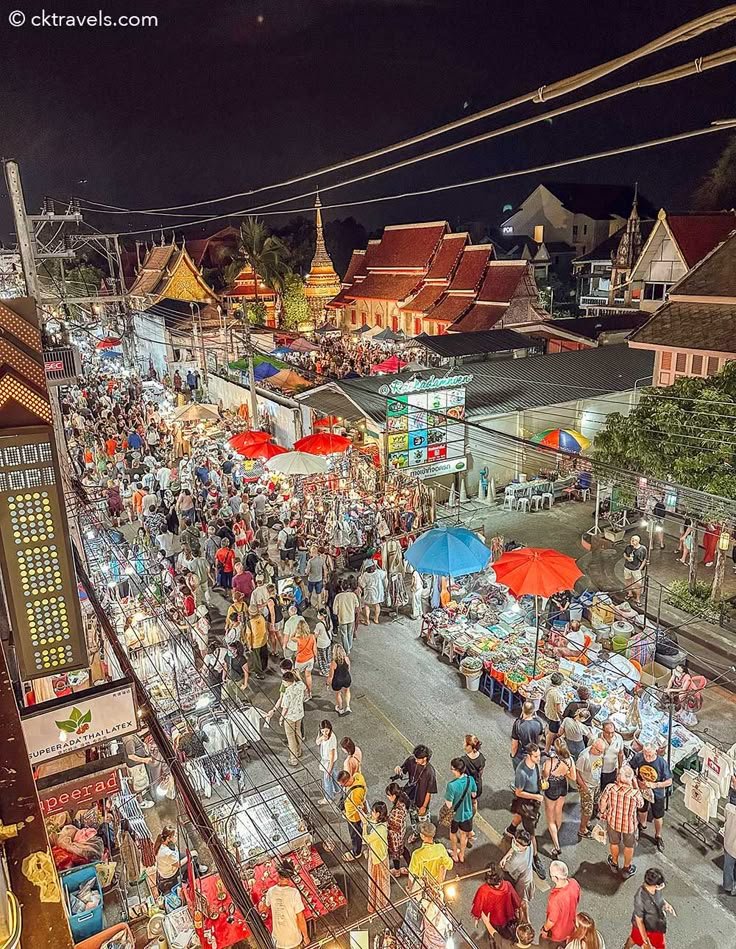 This may contain: an aerial view of people walking around in the city at night with umbrellas and food stalls