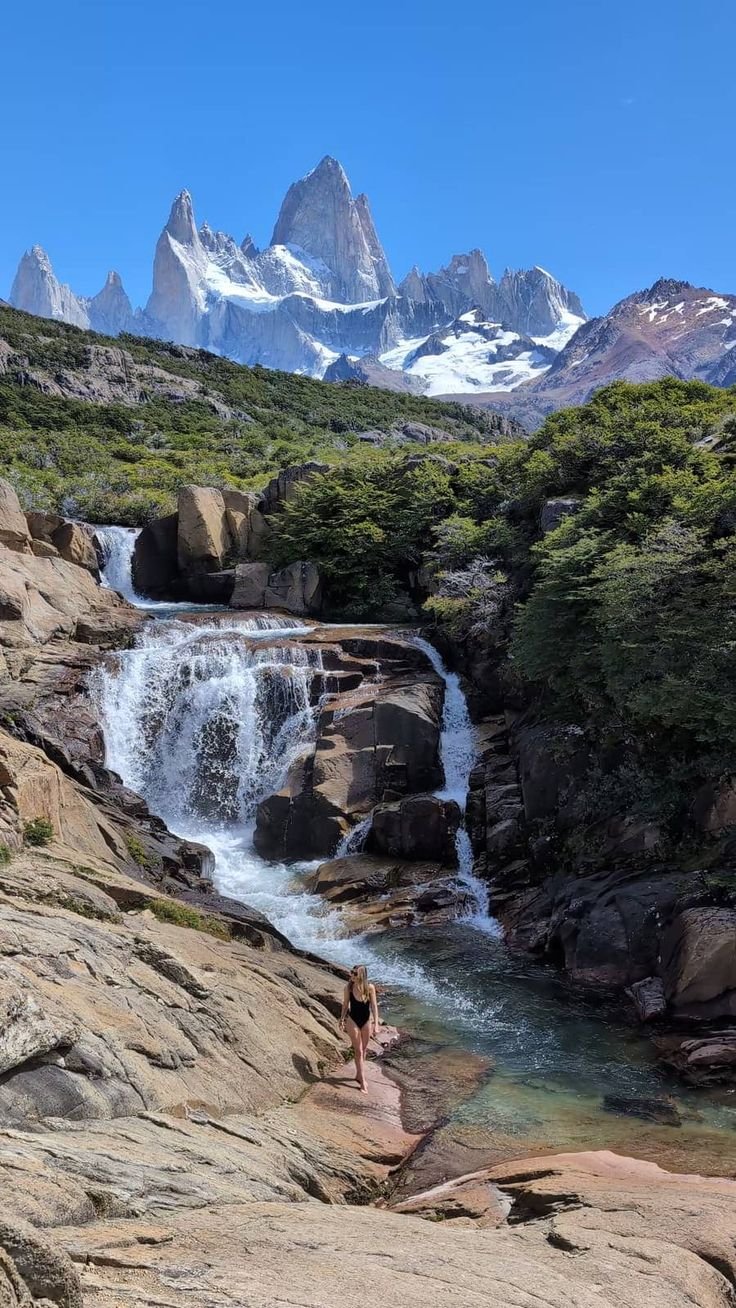 This may contain: a person standing on rocks near a waterfall