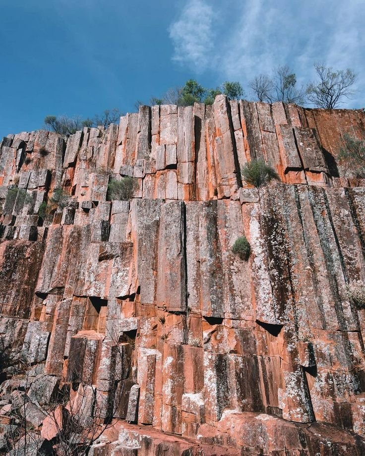 This may contain: a very tall rock wall with lots of rocks on it's sides and trees in the background